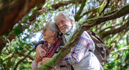 Senior couple together in a forest setting smiling enjoying nature and healthy lifestyle. Two retired man and woman embrace looking around symbolizing their close bond and happiness