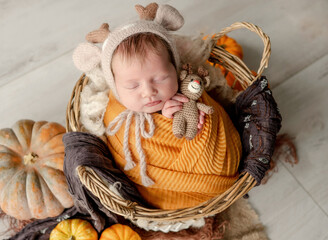 Newborn baby girl swaddled in white fabric sleeping in basket decorated with pumpkins. Infant child kid napping on fur autumn studio portrait