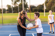 © Austockphoto - female netball coach encouraging a kid on the court who is learning to play netball