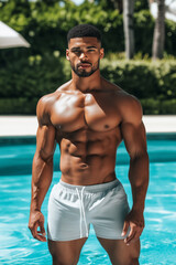 Wall Mural - Fit African American man in swim shorts, showcasing muscular physique by the swimming pool during a sunny summer vacation