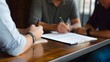 © Felippe Lopes - A close-up of three people's hands, as they sign documents during a business meeting.