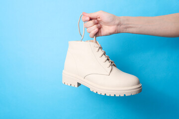 Wall Mural - Woman's hand holds a white leather shoe by the lace on a blue background