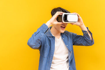 Asian young man in jacket jean and playing video games using vr with headphones on yellow background isolated.