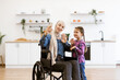 © sofiko14 - Bright kitchen background emphasizes family and connection. Muslim mother in wheelchair and daughter have video call, take selfie using phone, happily waving and smiling.