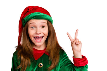 Sticker - Close up photo of cheerful festive elf kid with long red head haircut in green hat wearing elf costume making v-signs isolated over red background