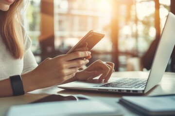 close-up shot of businesswoman using smart phone while working at home on laptop computer