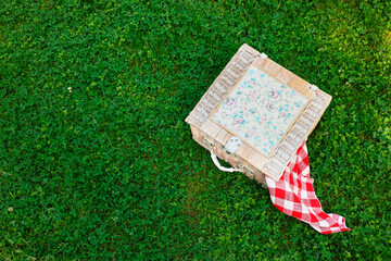 One picnic wicker basket with checkered napkin on green grass, above view. Space for text