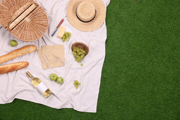 Wall Mural - Picnic basket, different snacks, wine and straw hat on green grass outdoors, top view. Space for text