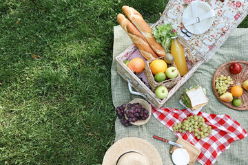 Poster - Picnic wicker basket with delicious food and drink on blanket outdoors, above view. Space for text