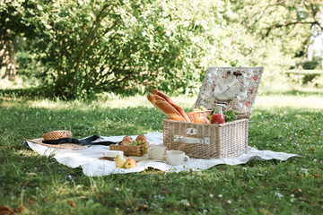 Wall Mural - Picnic wicker baskets with delicious food, tableware and drink on blanket outdoors