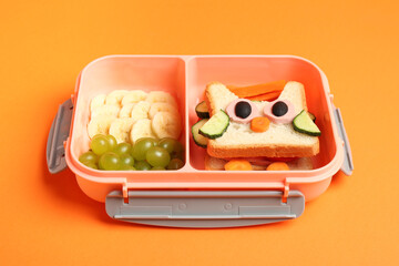 Canvas Print - Lunch box with sandwich and fruits on orange background