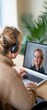 © Rona_65 - A woman engaged in a video call on her laptop, wearing headphones and sitting comfortably at her desk.