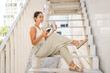 © Miljan Živković - Young happy woman sit on stairs drink coffee and use mobile phone