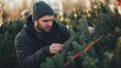© fotofabrika - Man carefully selecting a Christmas tree at a seasonal outdoor market in the early morning light