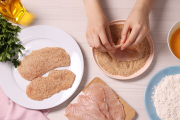 Wall Mural - Making schnitzel. Woman coating slice of meat with bread crumbs at white wooden table, top view