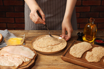 Poster - Woman making schnitzel at wooden table, closeup