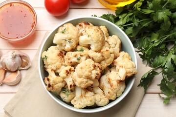 Wall Mural - Baked cauliflower in bowl, sauce and products on light wooden table, flat lay