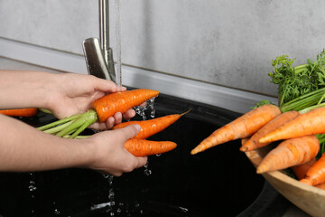 Sticker - Woman washing fresh carrots under tap water in above sink indoors, closeup