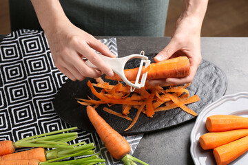 Wall Mural - Woman peeling fresh carrot at dark gray table, closeup