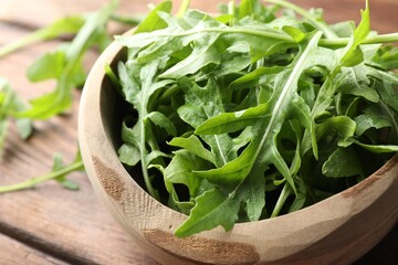 Wall Mural - Fresh green arugula leaves in bowl on wooden table, closeup