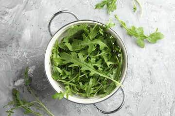 Sticker - Fresh green arugula leaves in colander on grey textured table, top view