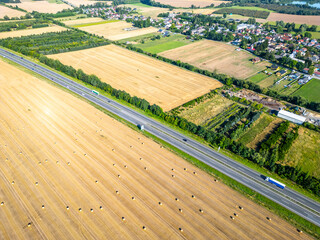 Overhead view of a field filled with hay bales adjacent to a highway, showcasing agricultural land and vehicles traveling.