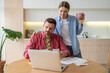 © DimaBerlin - Serious man manages family budget frown looks to unpaid bills sits with laptop wife stands beside watch by husband. Focused married couple check account in banking app find mistake at credit payment.