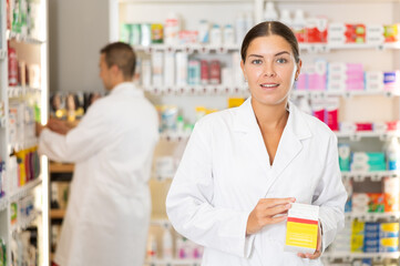 Wall Mural - Kind young apothecary holding a box with remedy standing against shelves full of medicine in drugstore