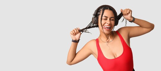 Wall Mural - Cool young African-American woman listening to music on light background with space for text