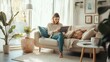 © fotofabrika - A woman relaxes on a cozy couch in a sunlit living room, enjoying her tablet on a serene afternoon surrounded by plants and decor