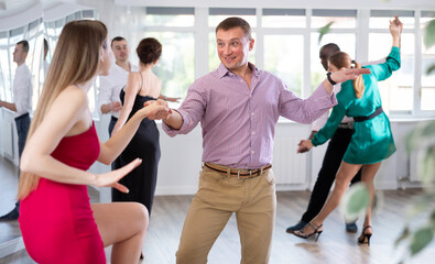 Positive woman and man dancing foxtrot in pair during group dance party