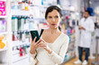 © JackF - Portrait of positive young adult woman consumer using smartphone at pharmacy