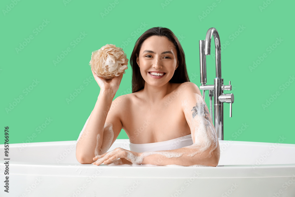Young woman with loofah taking bath on green background