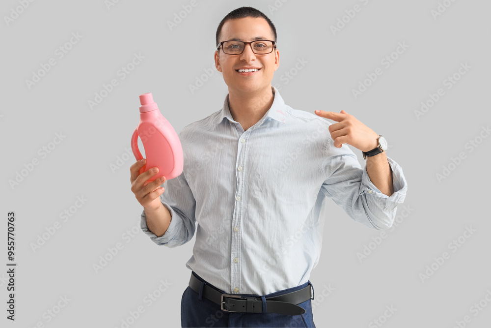 Young man pointing at bottle of laundry detergent on grey background
