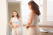 © Pixel-Shot - Sad young woman in tight pants near mirror at home. Weight gain concept