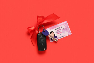 Gift keys of new car with bow and driver license on red background