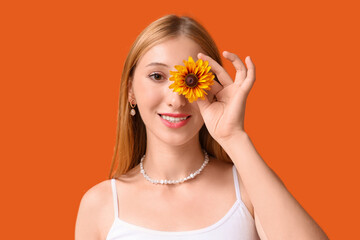 Wall Mural - Beautiful young happy woman in stylish outfit with flower on orange background