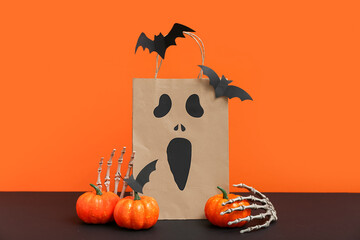 Paper shopping bag and decorations for Halloween on dark table against color background