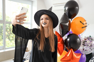 Poster - Young woman dressed for Halloween as witch with balloons taking selfie at home