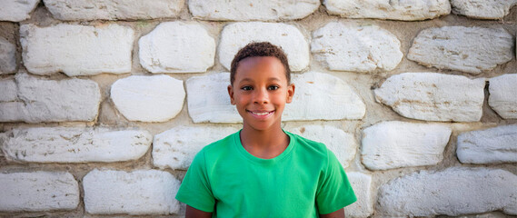 Wall Mural - A Black boy wearing a green T-shirt and laughing with his back against a stone wall