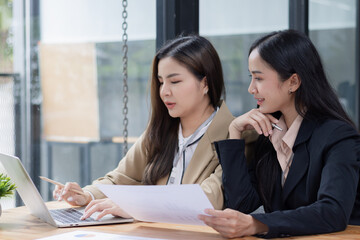 Two Asian businesswomen working on laptop computer with analyzing financial charts in the modern office, Business financial documents and planning idea project concept.