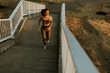 © BGStock72 - Determined woman jogs down sunlit stairs in athletic wear during a golden hour workout, enjoying the tranquility of nature in her daily routine