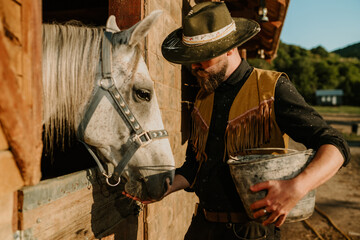 Wall Mural - Cowboy is feeding his horse at ranch near the stable.