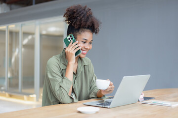 African American young woman using smartphone with laptop computer.