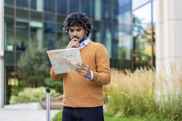 thoughtful man looking at city map while standing outdoors during sunny day. appears focused on plan