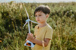 © Westend61 - Boy holding and staring at wind turbine model in field