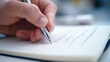 © D.e.a.r - A close up of persons hand writing in notebook, capturing focus and creativity involved in process.
