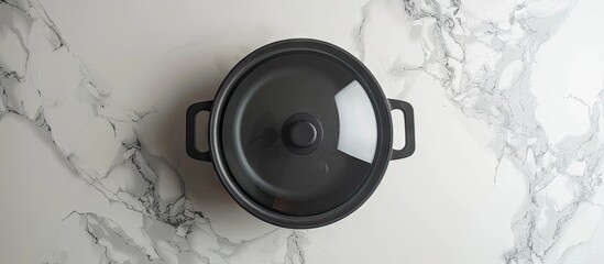 Poster - Top view of a black cooking pot with a transparent lid placed on a white marble surface offering a clear area for including text within the image. Creative banner. Copyspace image