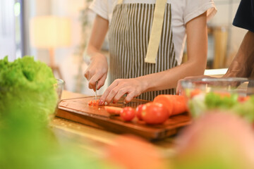 Wall Mural - Young woman chopping tomatoes on a wooden cutting board preparing healthy meal in kitchen