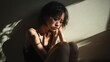 © niti - Asian woman sitting on the floor in a corner, knees pulled to her chest, face buried in her arms, shadows surrounding her, guilt expression, despair and isolation